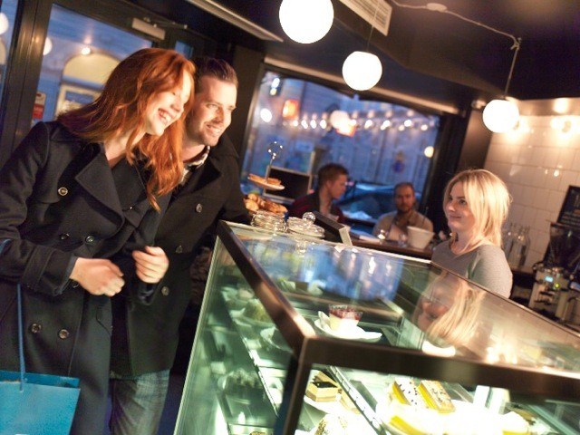 Guests at a café display counter under warm globe lights.