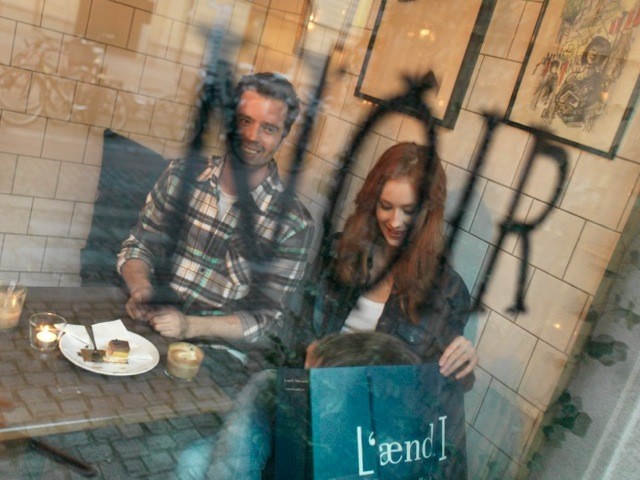 Two guests sharing coffee and cake, seen through the lettering on a café window.