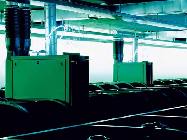 Rows of gaming stations beneath exposed pipes and blue-green lighting at Gamer’s Paradise.